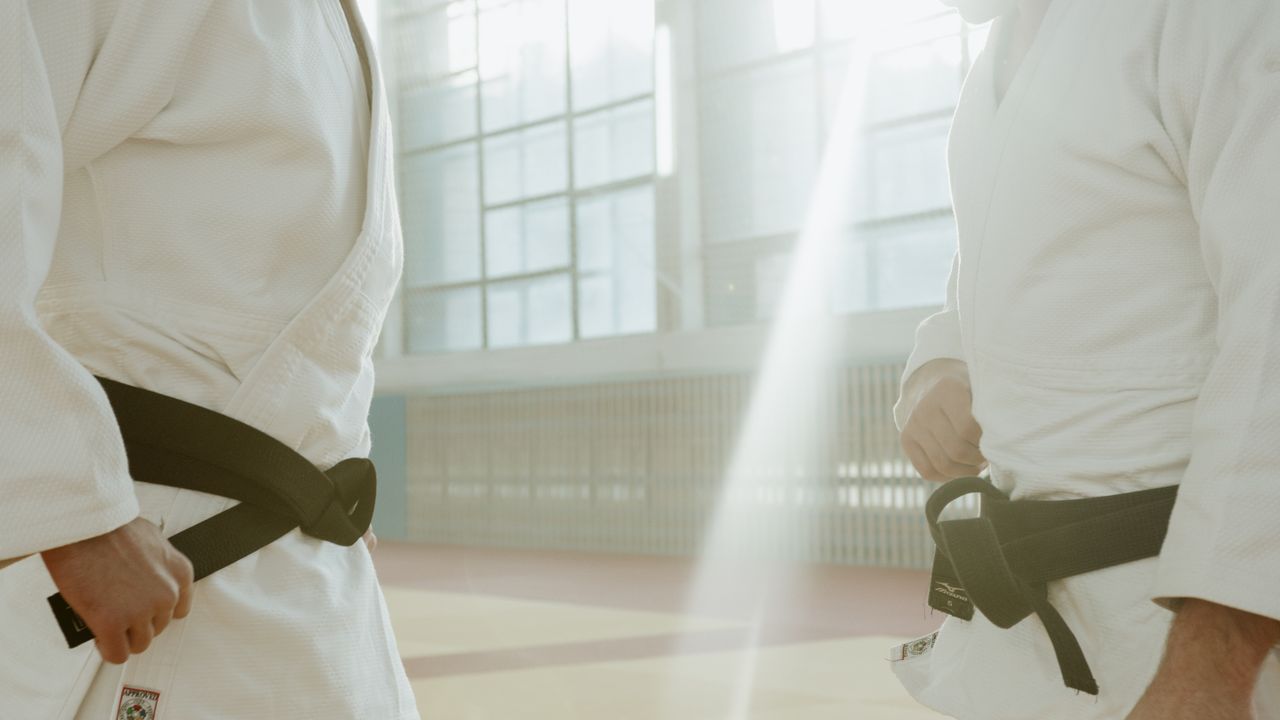 Two martial artists in white uniforms preparing for practice in a well-lit indoor gym.