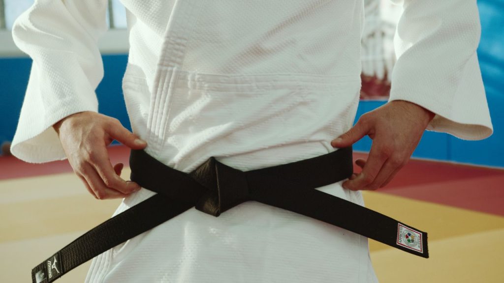 Close-up of a martial artist tying a black belt, symbolizing expertise and discipline.