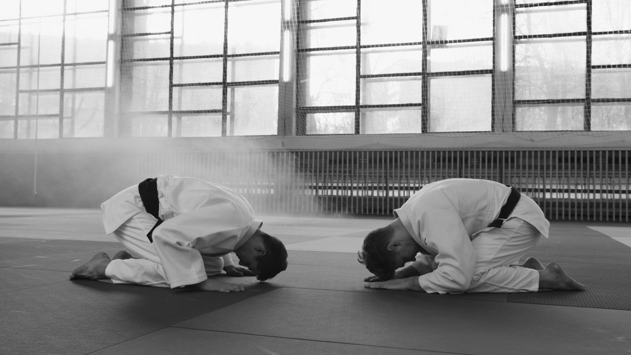 Two martial artists in training hall bowing as a sign of respect, grayscale image.
